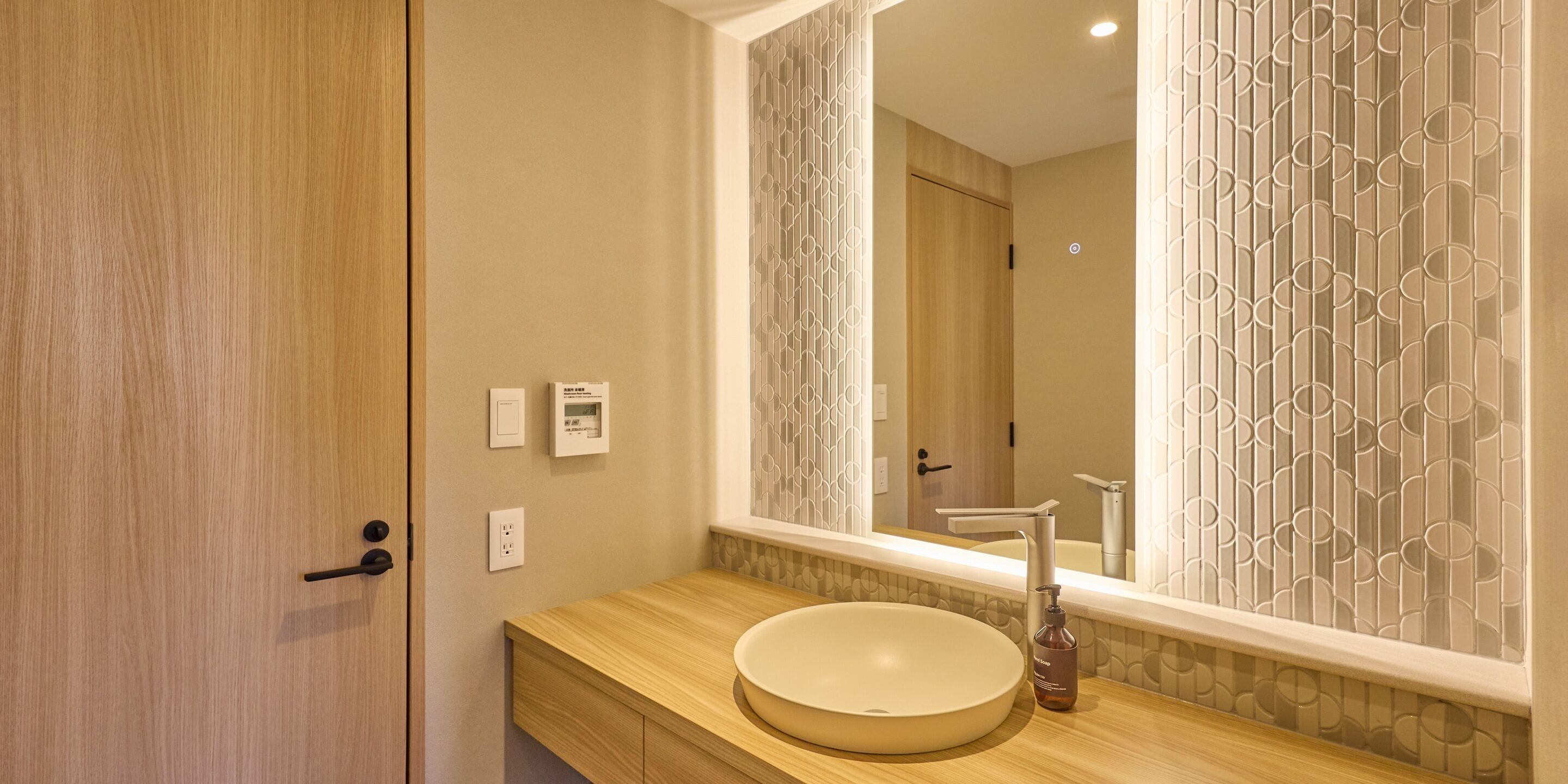 Un baño con tocador de madera, un lavabo redondo, un espejo y una puerta con pomo.