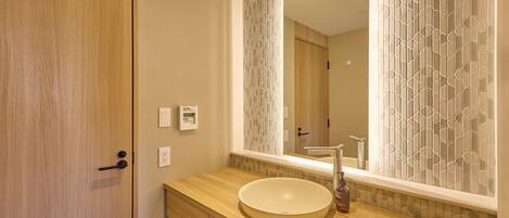 Un baño con tocador de madera, un lavabo redondo, un espejo y una puerta con pomo.