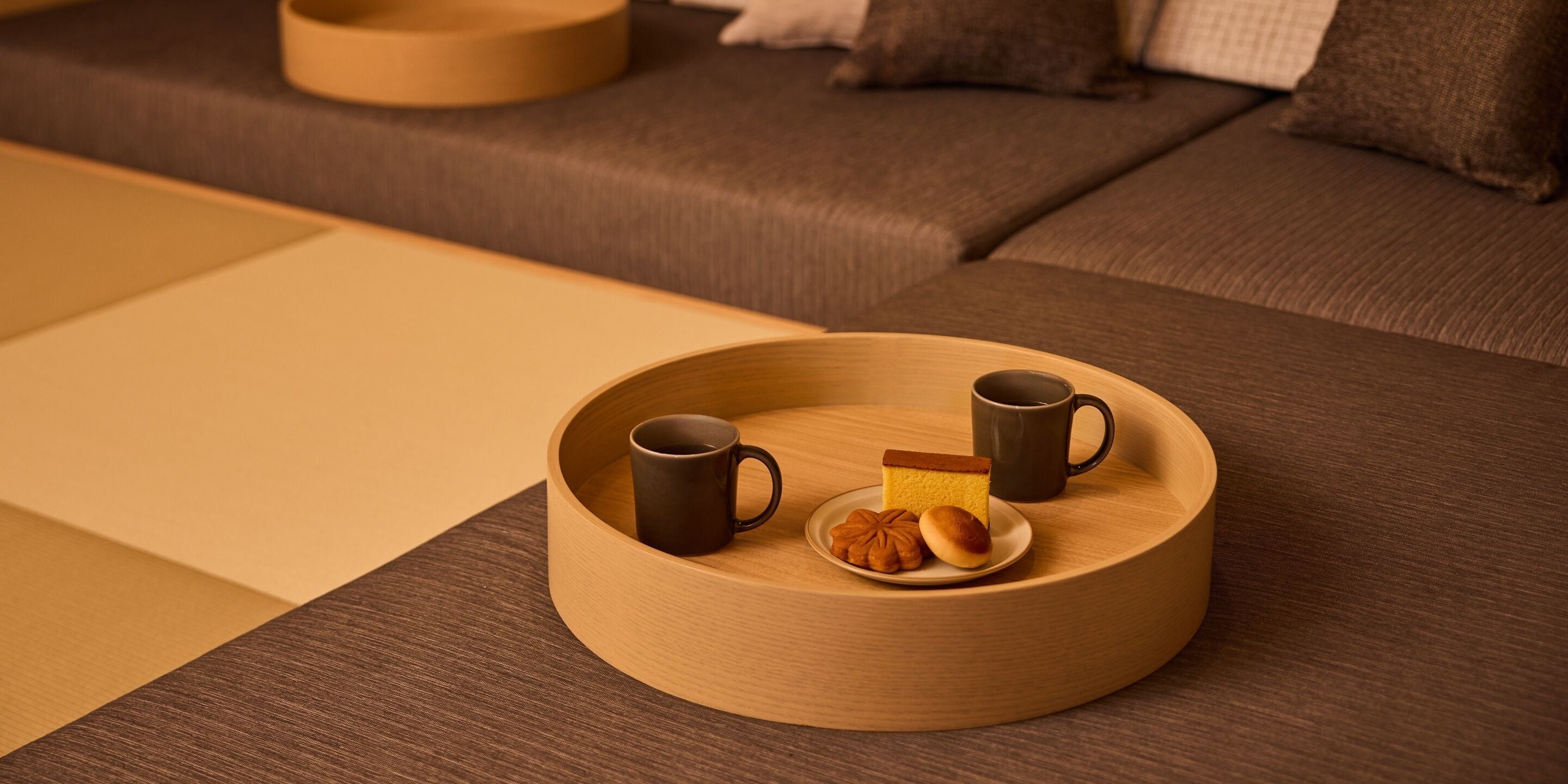 Ein runder Holztisch mit zwei Tassen und einem Teller Gebäck auf einer Couch.