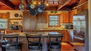 Une cuisine avec des meubles en bois, un réfrigérateur en acier inoxydable, des casseroles suspendues et un coin bar avec des tabourets.