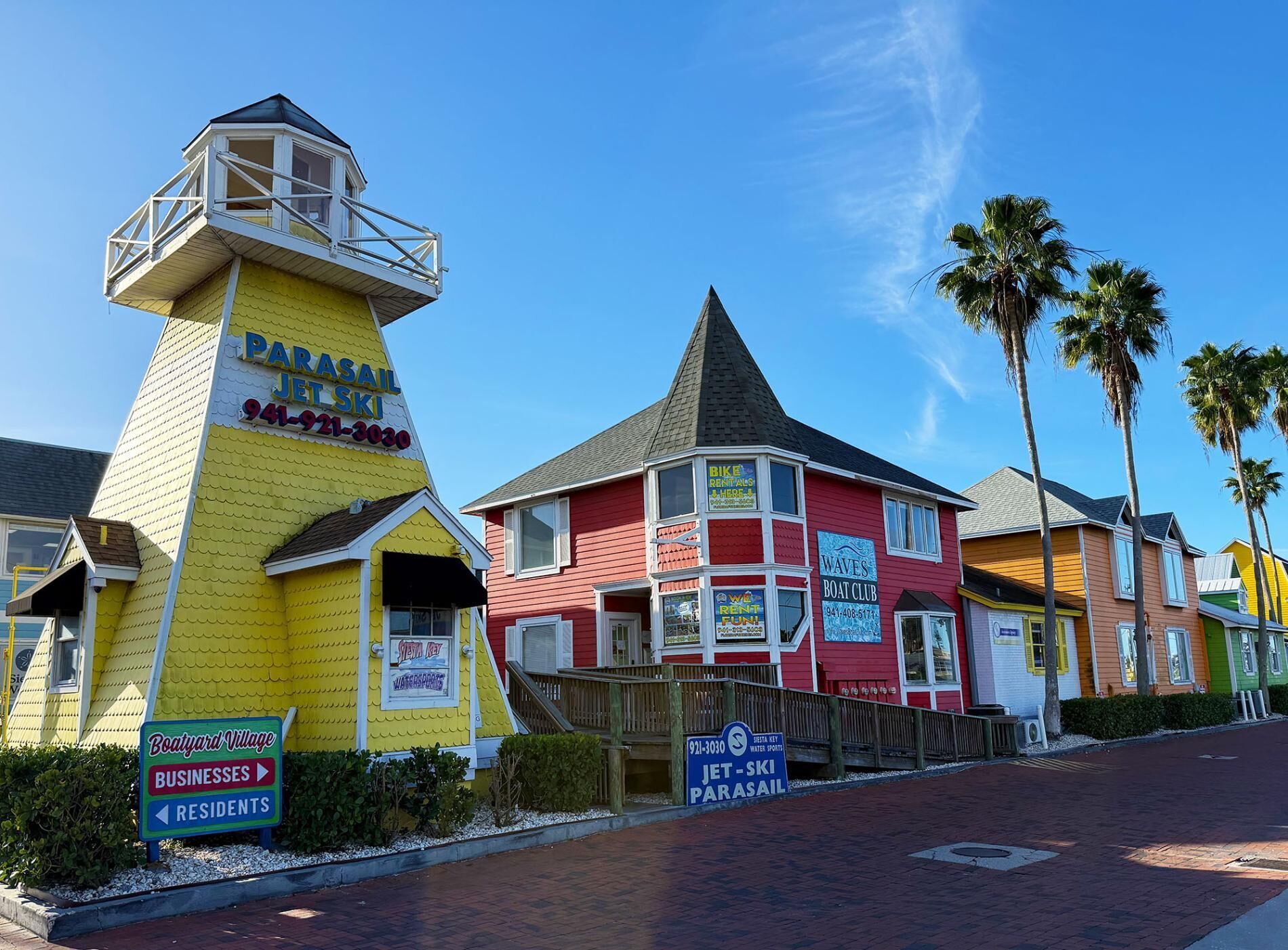 A colorful building with a lighthouse-like structure, a red building with a boat club sign, and a sign for Jet-Ski Parasail.