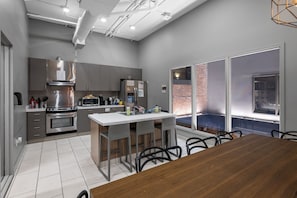 Une cuisine moderne avec des meubles gris, des appareils en acier inoxydable et un grand îlot central doté de tabourets de bar.