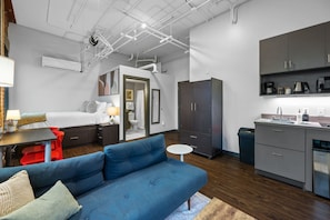 A compact living space with a blue sofa, a small dining table, a kitchenette with dark cabinets, and a separate bathroom.