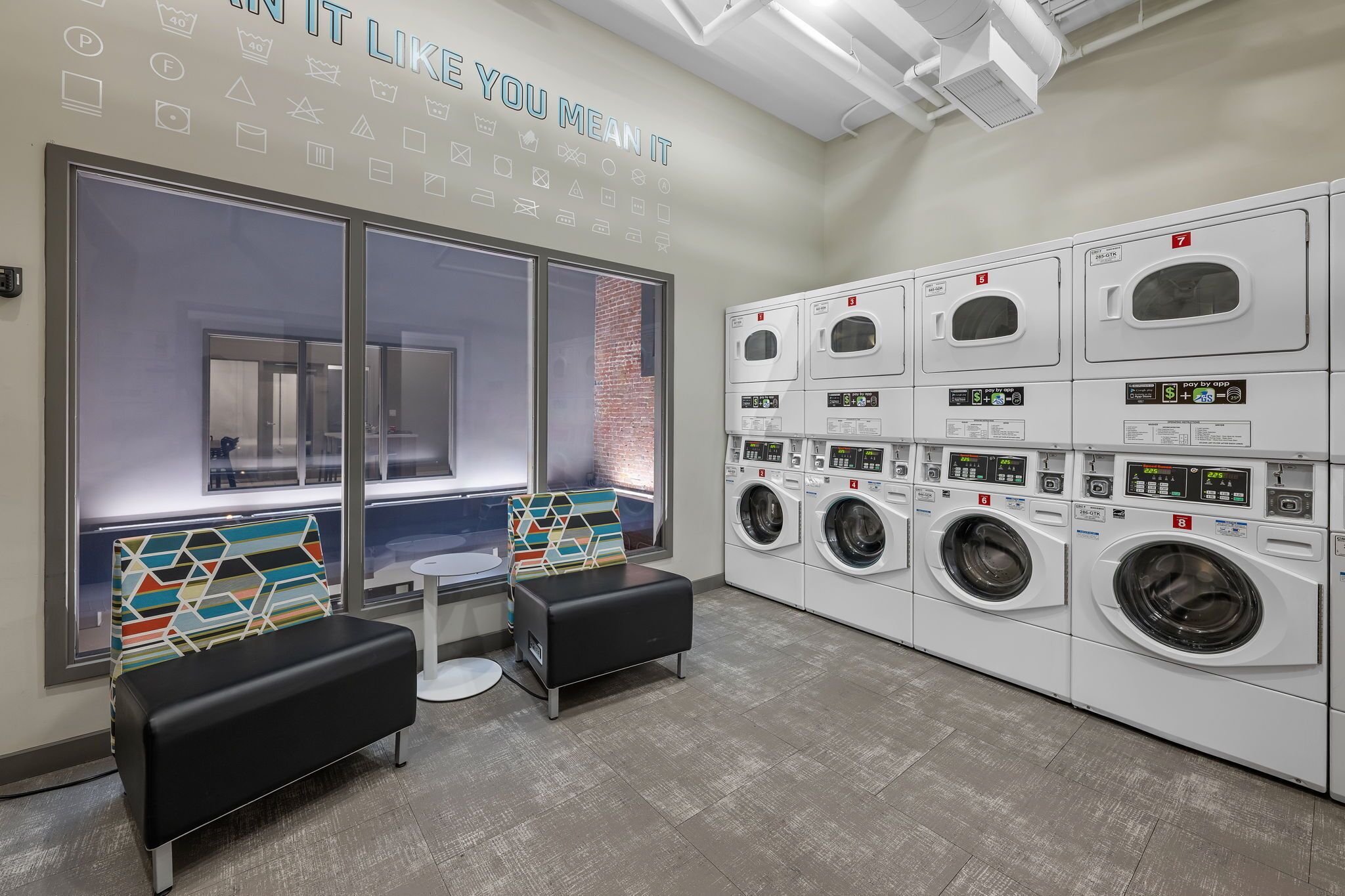A laundry room with multiple washing machines, a bench, and a window with a view.