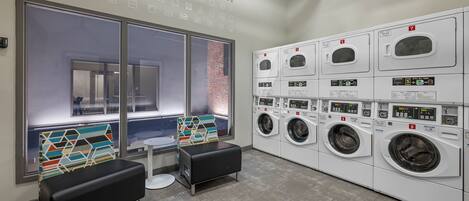 A laundry room with multiple washing machines, a bench, and a window with a view.