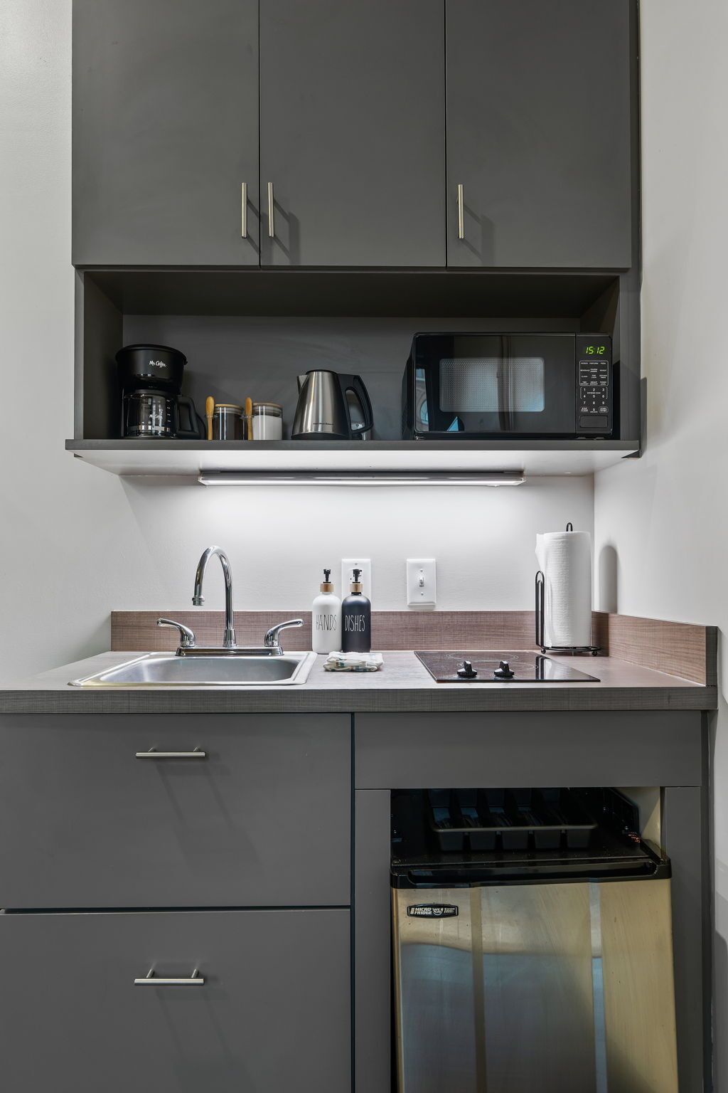 A modern kitchen with grey cabinets, a stainless steel dishwasher, a microwave, and a coffee maker.