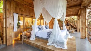 Una habitación lujosa con cama a dosel, paredes de bambú y una escalera que conduce a un nivel superior.