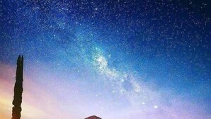 Escena nocturna con cielo estrellado, una montaña al fondo y un edificio iluminado con escalones que lo llevan a él.