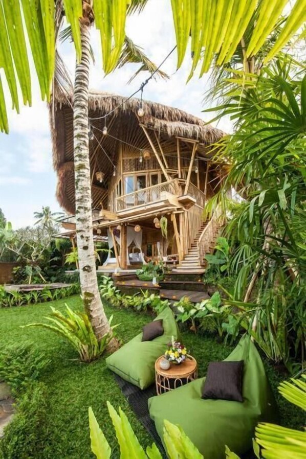 Una casa con techo de paja y escalera de madera, rodeada de exuberante follaje y un césped cuidado.