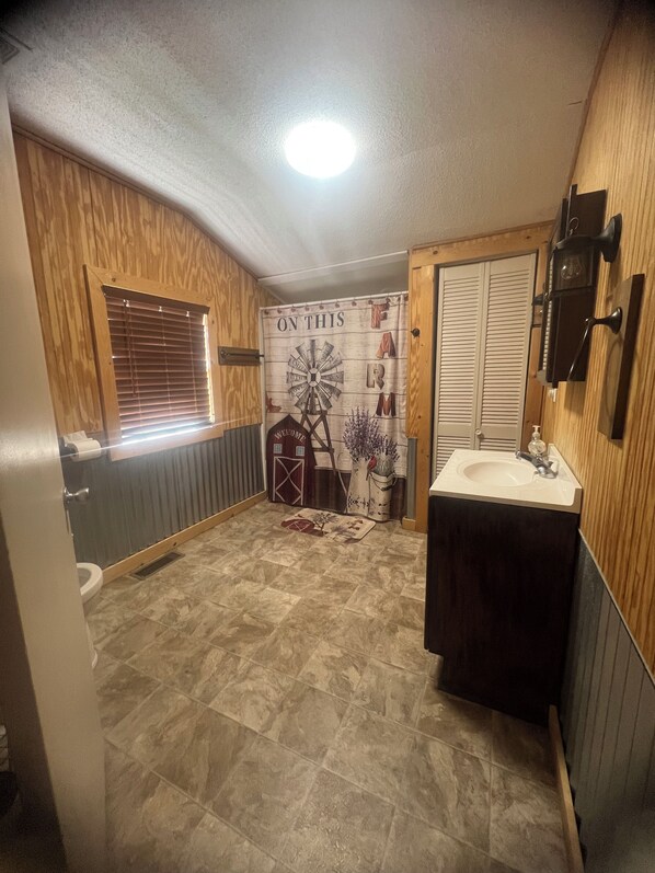 A bathroom with a wooden wall, a white sink, and a window with blinds.