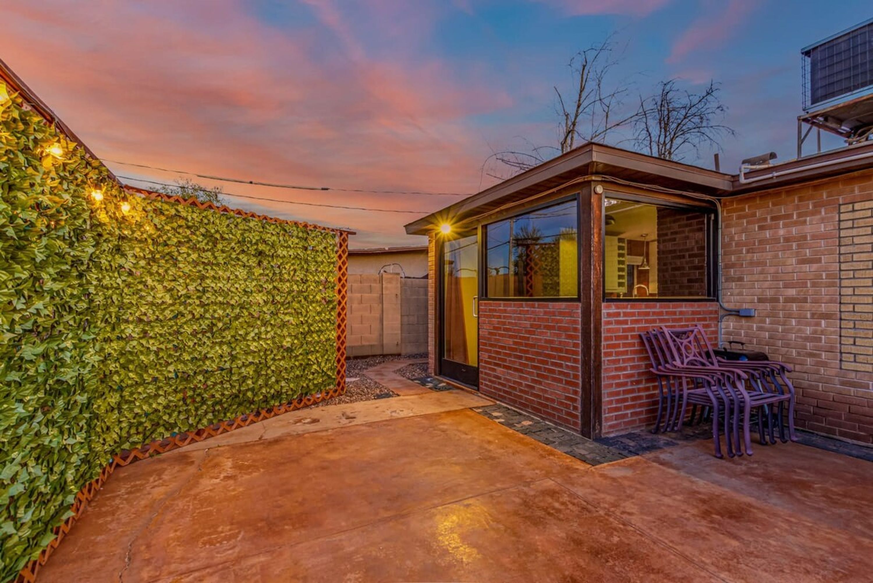 Une terrasse avec un mur en briques, une véranda en verre et un espace détente avec des chaises.
