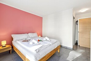 A neatly made bed with white linens and pillows, a bedside lamp, and a small table with a book and a flower. - Locarno Centro Apartment, Locarno, Switzerland (Locarno)