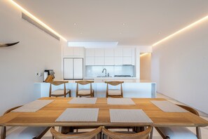 A modern kitchen with white cabinets, a central island, and a dining area with a wooden table and chairs. - New Luxury Oceanview Golf Resort, Pool and Hot-tub (San José del Cabo)