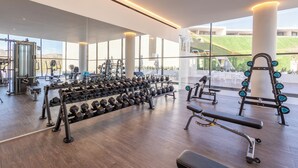 Et moderne fitnesscenter med forskelligt styrketræningsudstyr, store vinduer og udsigt til det fri.