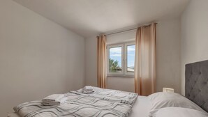 Ein ordentlich bezogenes Bett mit einem gestreiften Bettüberwurf, ein Fenster mit Vorhängen und ein Nachttisch mit einer Lampe.