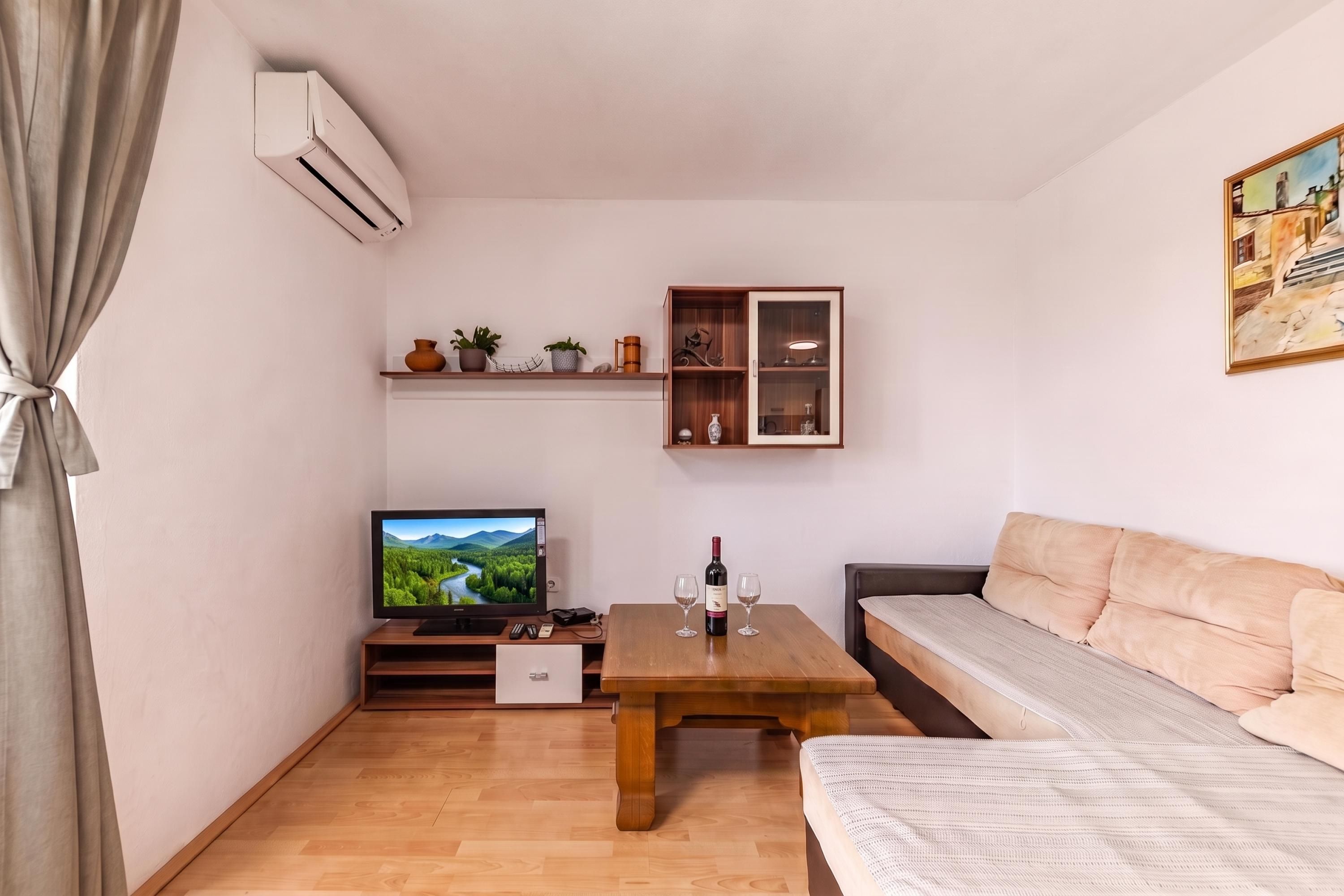 Una sala pequeña con televisor, una mesa de centro de madera, un sofá y un mueble con objetos decorativos.