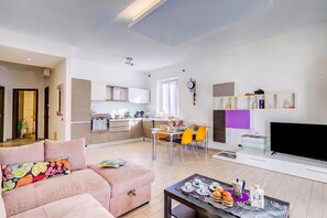 Ein modernes Wohnzimmer mit einer Couch, einem Essbereich mit Stühlen, einer Küche mit Schränken und einem an der Wand befestigten Flachbildfernseher.