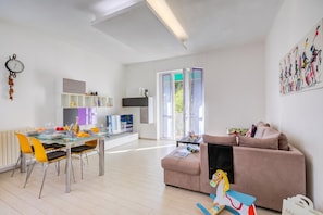 Ein modernes Wohnzimmer mit einer Couch, einem Essbereich mit Stühlen und einem Tisch, einem Fernseher und einer Uhr an der Wand.