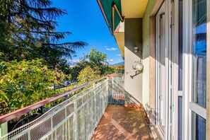 Ein Balkon mit Metallgeländer, Blick auf Bäume und Berge sowie ein Gebäude mit grüner Markise.