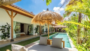 A poolside area with a wooden deck, lounge chairs, and a thatched umbrella. - Tropical escape - 4bdrs villa in Bingin Beach (Pecatu, South Kuta, Badung Regency,)