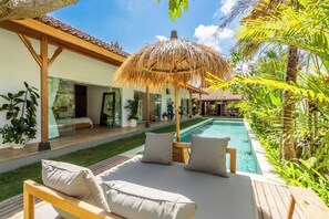 A poolside area with a wooden deck, lounge chairs, and a thatched umbrella. - Tropical escape - 4bdrs villa in Bingin Beach (Pecatu, South Kuta, Badung Regency,)