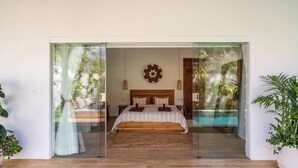A bedroom with a large bed, a wooden headboard, and a view of a pool through a glass door. - Tropical escape - 4bdrs villa in Bingin Beach (Pecatu, South Kuta, Badung Regency,)