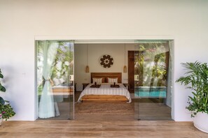 A bedroom with a large bed, a wooden headboard, and a view of a pool through a glass door. - Tropical escape - 4bdrs villa in Bingin Beach (Pecatu, South Kuta, Badung Regency,)
