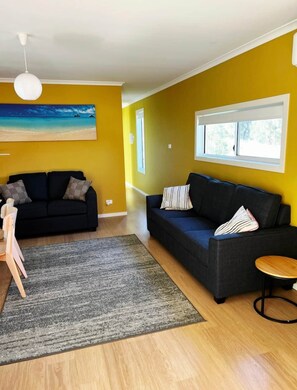 A living room with two sofas, a rug, a painting, and a window. - Bruny Seaview Escape Alonnah (Alonnah)