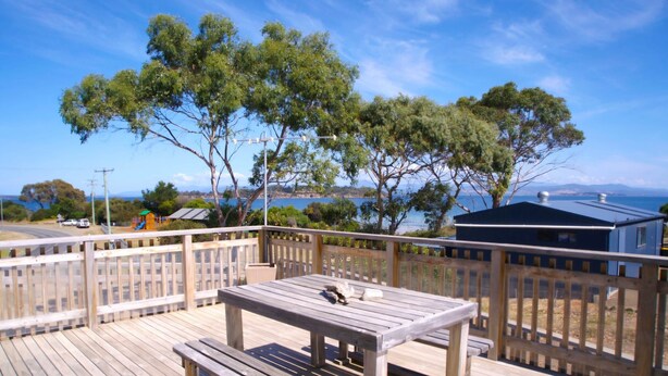 A wooden deck with a table and bench, overlooking a scenic view of trees and a body of water. - Bruny Seaview Escape Alonnah (Alonnah)