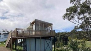 A single-story building with a wooden deck and a covered area, surrounded by a gravel path and greenery. - Bruny Seaview Escape Alonnah (Alonnah)