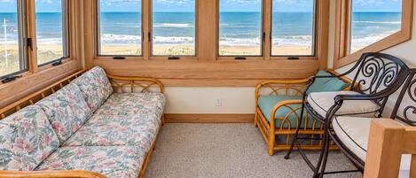 A room with a view of the beach, a sofa, a chair, and a small table.
