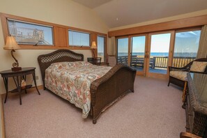 A bedroom with a large bed, a small table, a chair, and a view of the beach through large sliding doors. - AMES - 4 BR Oceanfront home w/Ocean Views & Elevator (Southern Shores)