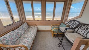 A room with a sofa, a chair, and a table, with large windows overlooking a beach. - AMES - 4 BR Oceanfront home w/Ocean Views & Elevator (Southern Shores)