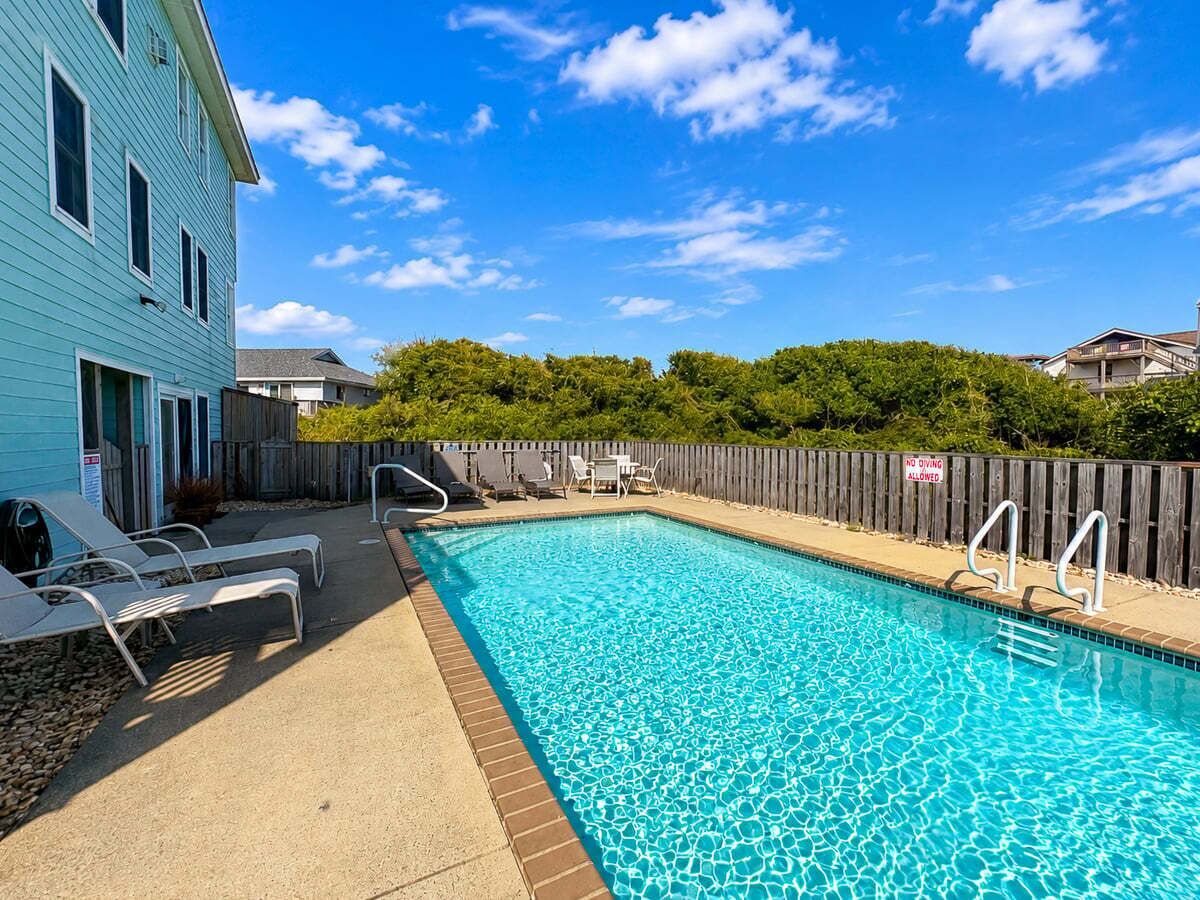 A swimming pool with lounge chairs and a wooden fence.