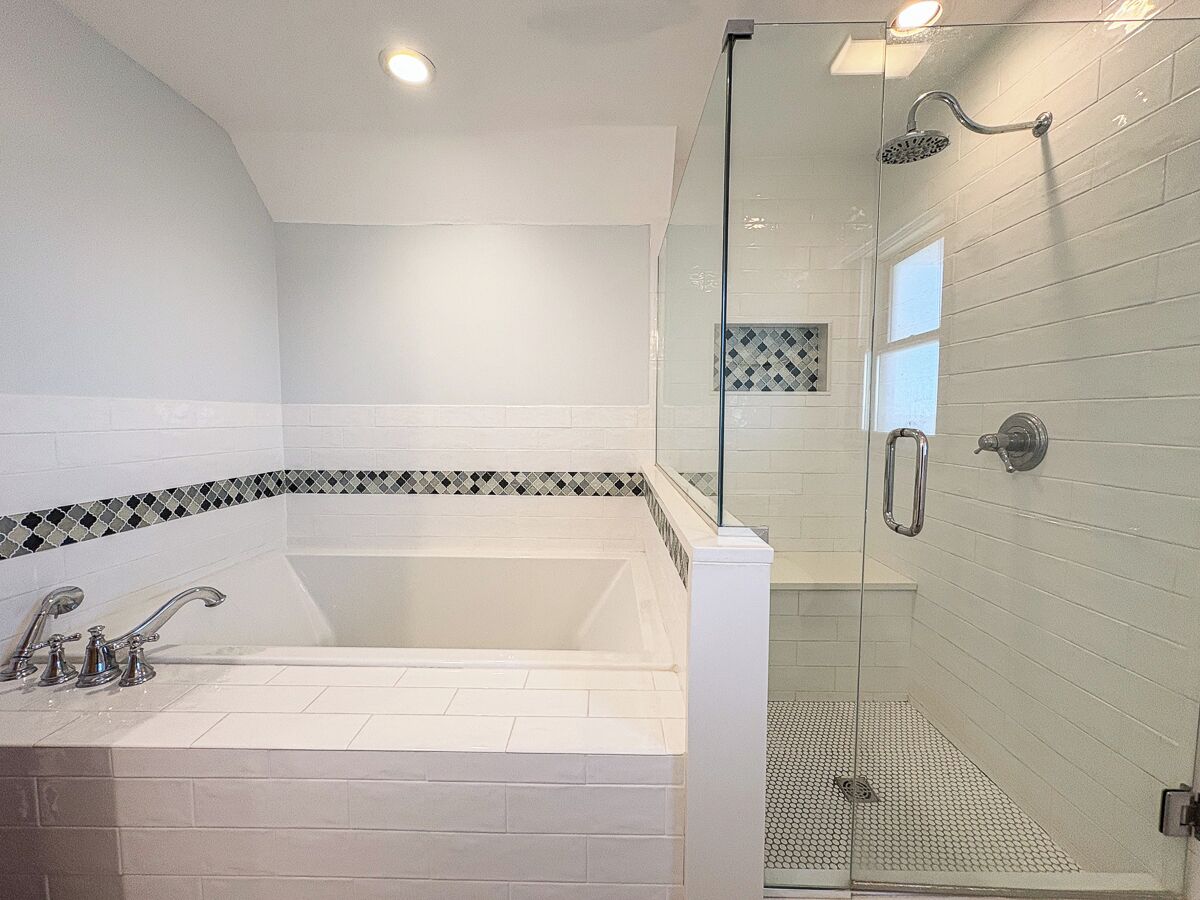 Een moderne badkamer met een vrijstaand bad, een douche met glazen wand en een betegelde vloer.