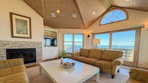 Una sala de estar acogedora con chimenea, un ventanal con vistas al océano y una zona de estar confortable.
