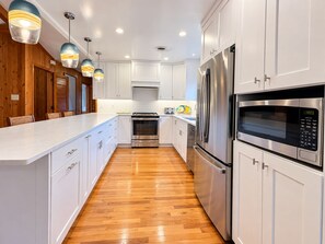 A modern kitchen with white cabinetry, stainless steel appliances, and a wooden floor. - FUNNY DUCK - 4 BR Oceanside Home w/Private Pool (Duck)
