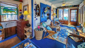 Una stanza con arredamento nei toni del blu e del bianco, che include un settimino in legno, mobili in vimini e un'ampia finestra con vista.
