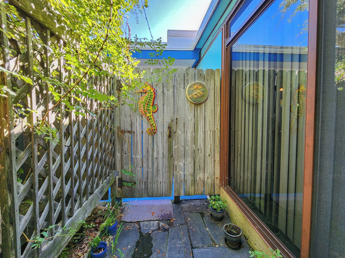 A wooden fence with a decorative metal piece, a small step leading to a door, and potted plants on the ground.