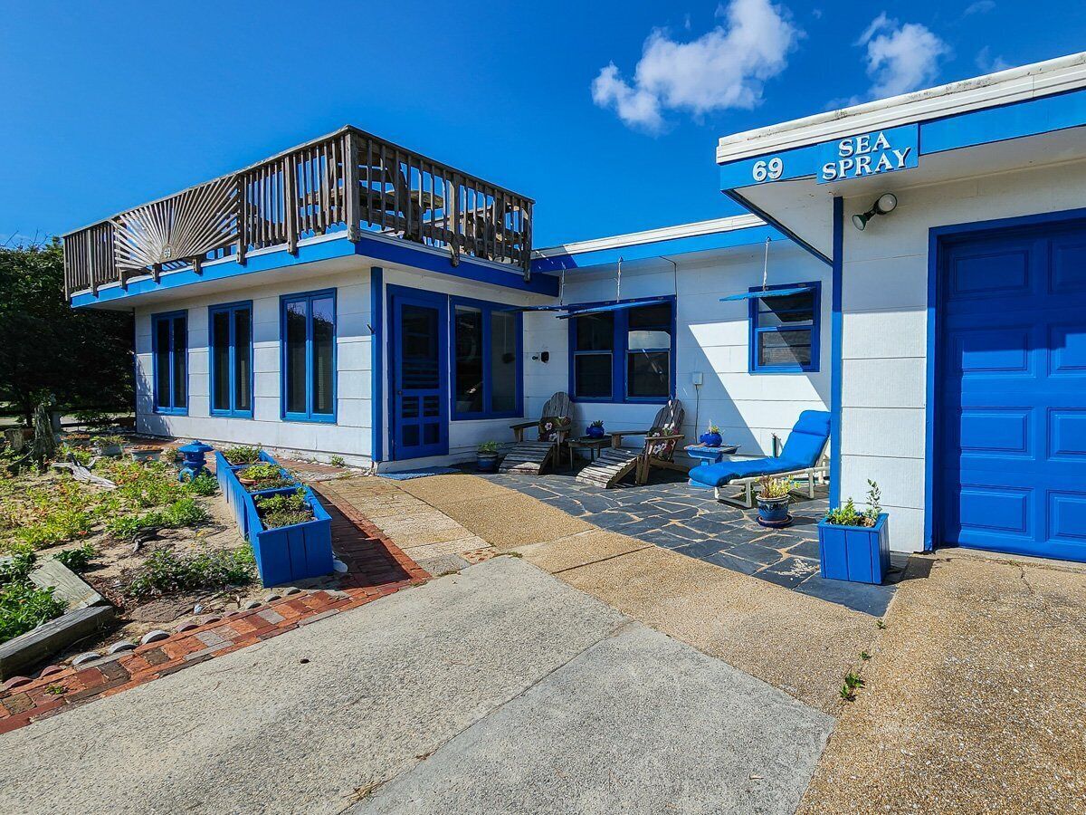 Um edifício com fachada azul e branca, uma área de estar coberta ao ar livre e uma placa com a inscrição 'SEA SPRAY'.