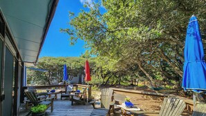 Un terrazzo in legno con sedute all'aperto, ombrelloni e vista sugli alberi.