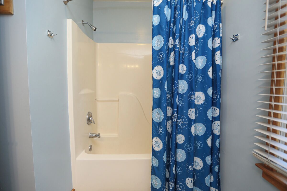 A bathroom with a bathtub, a shower curtain, and a window with blinds.