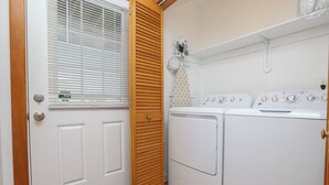Een wasserette met een wasmachine en droger, een houten deur en een raam met zonwering.