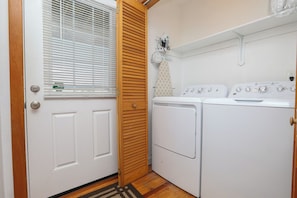 A laundry room with a washing machine and dryer, a wooden door, and a window with blinds. - SNOW GOOSE - 4 BR Semi-Oceanfront Home, Just 1 Lot From The Ocean (Duck)