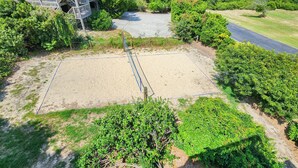 Een zandvolleybalveld omgeven door weelderige begroeiing, met een trap die naar een gebouw in de verte leidt.