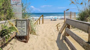 Een strandpad dat naar de oceaan leidt, met een bord waarop staat dat barbecues of vuurwerk verboden zijn.