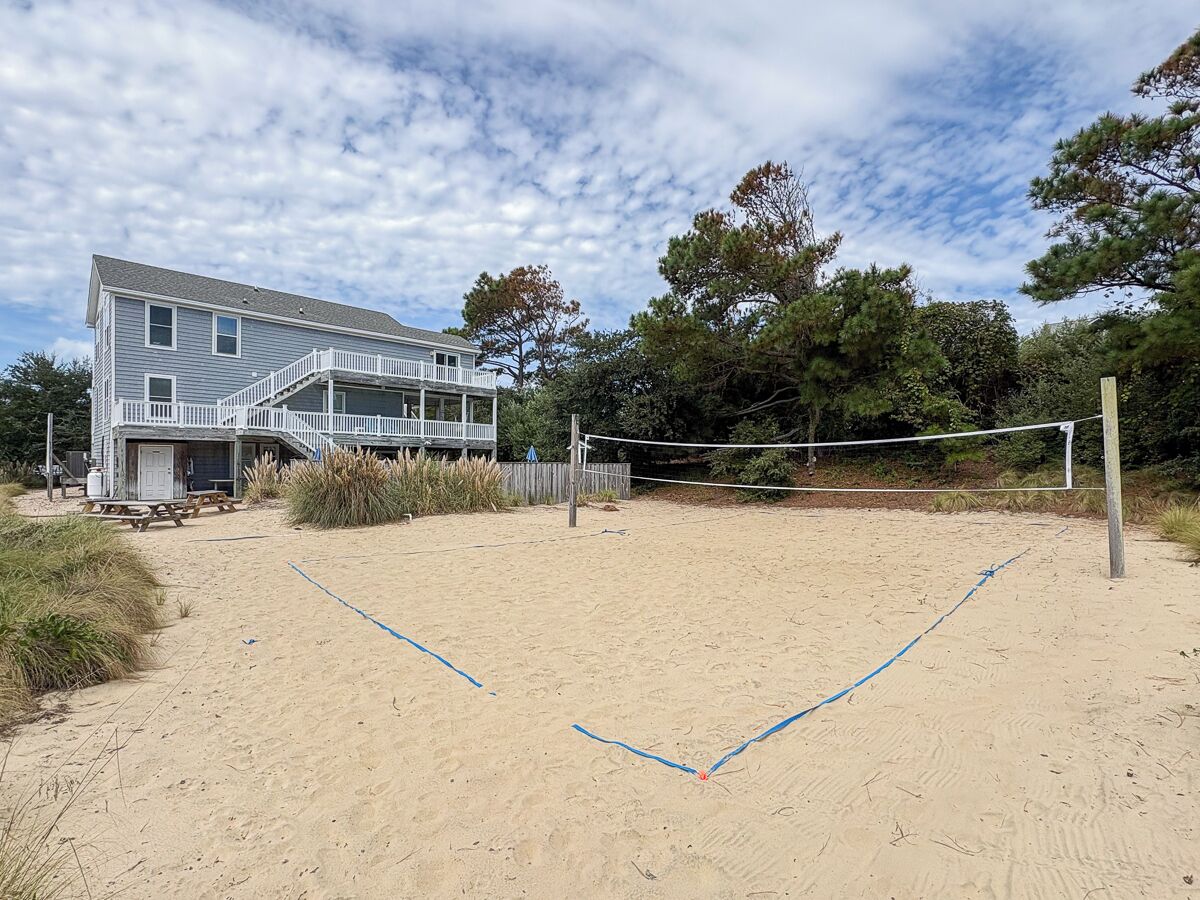 A beach volleyball court with a net, a wooden fence, and a house in the background.