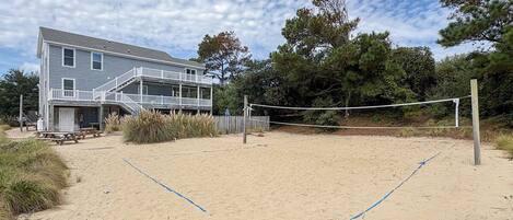 A beach volleyball court with a net, a wooden fence, and a house in the background.