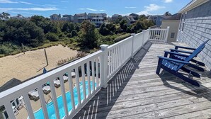 A wooden deck with a pool, lounge chairs, and a view of a beach and houses. - DOLPHIN DUNES - 7 BR Oceanside Retreat In DUCK - Pool, Dogs allowed (Duck)