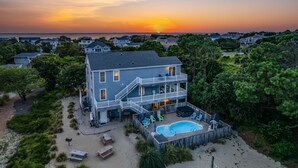 A two-story house with a pool and outdoor seating area, surrounded by trees and a beach view. - DOLPHIN DUNES - 7 BR Oceanside Retreat In DUCK - Pool, Dogs allowed (Duck)